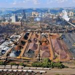 Vista ampla de uma instalação mineradora industrial, com máquinas, estruturas de processamento e pilhas de resíduos minerais.