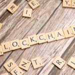Letras de madeira formando a palavra “blockchain” sobre uma superfície de madeira.