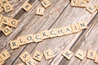 Letras de madeira formando a palavra “blockchain” sobre uma superfície de madeira.